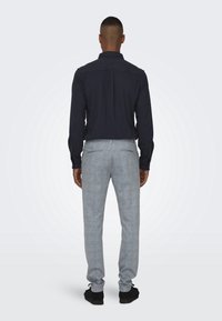 Camisa de botones navy de manga larga, combinada con pantalones de rayas en gris claro. El conjunto presenta un corte clásico y texturas sutiles.