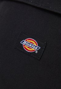 Fekete szövet folt a "Dickies" logóval; kör alakú dizájn piros és sárga kiegészítőkkel, kék betűzés strukturált háttéren.