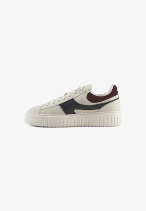 Sneakers met een lichtbeige leren bovenkant, een donkerbruine suède hakaccent, een zwart zijlogo en een dikke witte rubberen zool. Platte veters.