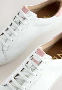 Baskets en cuir blanc avec des lacets blancs et des accents en daim rose sur la languette et le talon, vues de dessus.