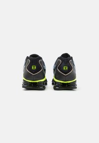 Musta urheilukengät, joissa on teksturoitu päällinen, sininen kuvio, neonvihreät yksityiskohdat ja kiiltävä musta pohja iskunvaimennuselementeillä.