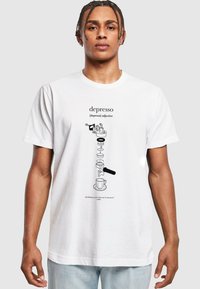 T-shirt en coton blanc présentant une illustration graphique noire avec le mot "depresso" et des images et du texte associés au café en dessous.