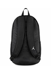 Mochila negra con correas ajustables acolchadas, tela texturizada y un detalle de logo blanco en la parte inferior derecha. Presenta un diseño sutil en relieve.