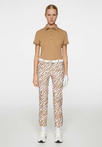 Brun pikétröja med korta ärmar och treknappslinning, kombinerad med vita byxor med ett brunt zickzackmönster. Vitt skärp och handskar.