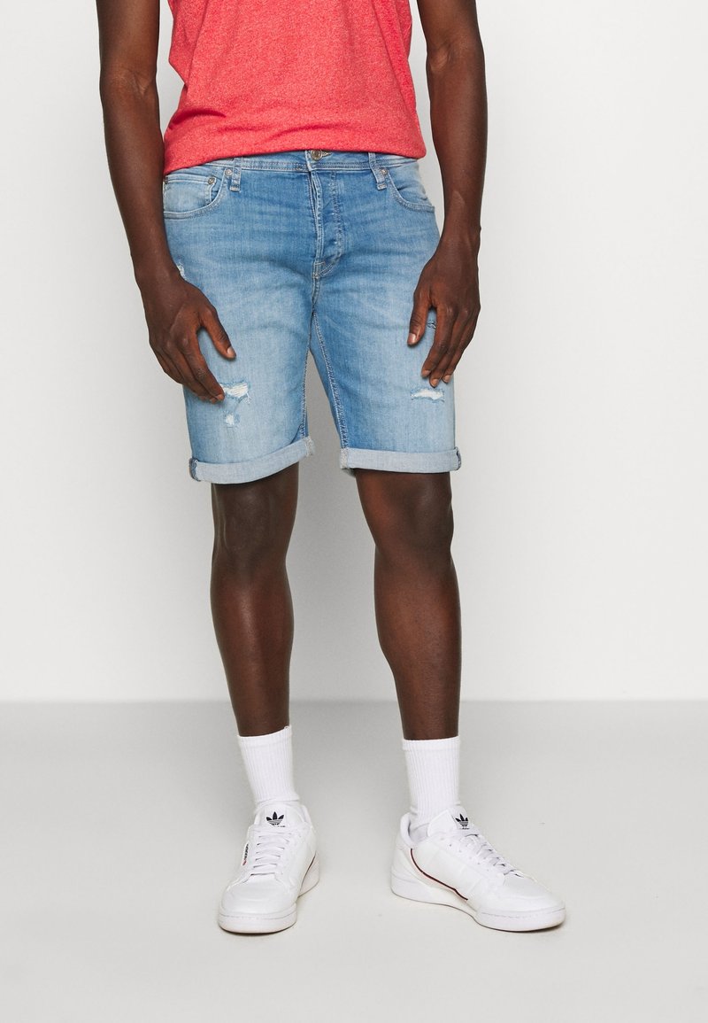 Světlé modré džíny s ohrnutými manžetami, které mají přední kapsy a zdobení v podobě oděrek. Nosí se s červenou košilí a bílými teniskami.