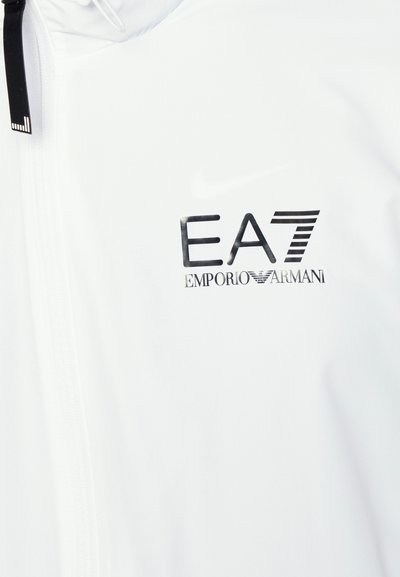Бяла жакет с цип и гладка текстура, с черно лого EA7 Emporio Armani отпред. Дърпачът на ципа има малък черен акцент.