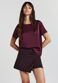 Top corto bordeaux in tessuto morbido, abbinato a una mini gonna scura con design avvolgente e linee pulite. Entrambi i capi sono eleganti.