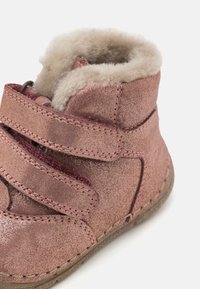 Růžová metalická kotníková bota s jemným béžovým podšívkou, dvěma suchými zipy a viditelným švem. Kulatá špička a flexibilní gumová podrážka.