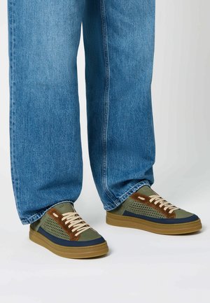 Green and navy sneakers with perforated design, brown suede accents, beige laces, and rubber soles, paired with light blue jeans.