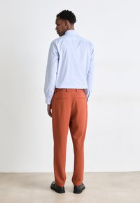 Chemise boutonnée rayée bleue, pantalon orange texturé et chaussures noires. Vue de dos, mettant en valeur les détails et l'ajustement du vêtement.