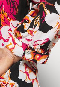 Camicia a stampa floreale caratterizzata da colori nero, bianco, rosa e arancione. Tessuto morbido con dettagli sui polsini a bottone e design delle maniche gather.