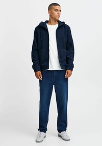 Marineblauwe fleece hoodie met voorzakken, ritsluiting en trekkers. Gecombineerd met donkerblauwe jeans en grijze sneakers. Casual pasvorm en ontwerp.