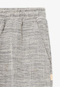 Pantalon en tissu tissé avec un motif texturé en crème et bleu marine. Dispose d'une taille élastique et de poches latérales. Petite étiquette de marque visible.