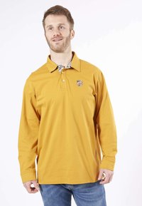 Polo à manches longues en coton jaune moutarde, avec un col à motif et un logo brodé sur la poitrine gauche.