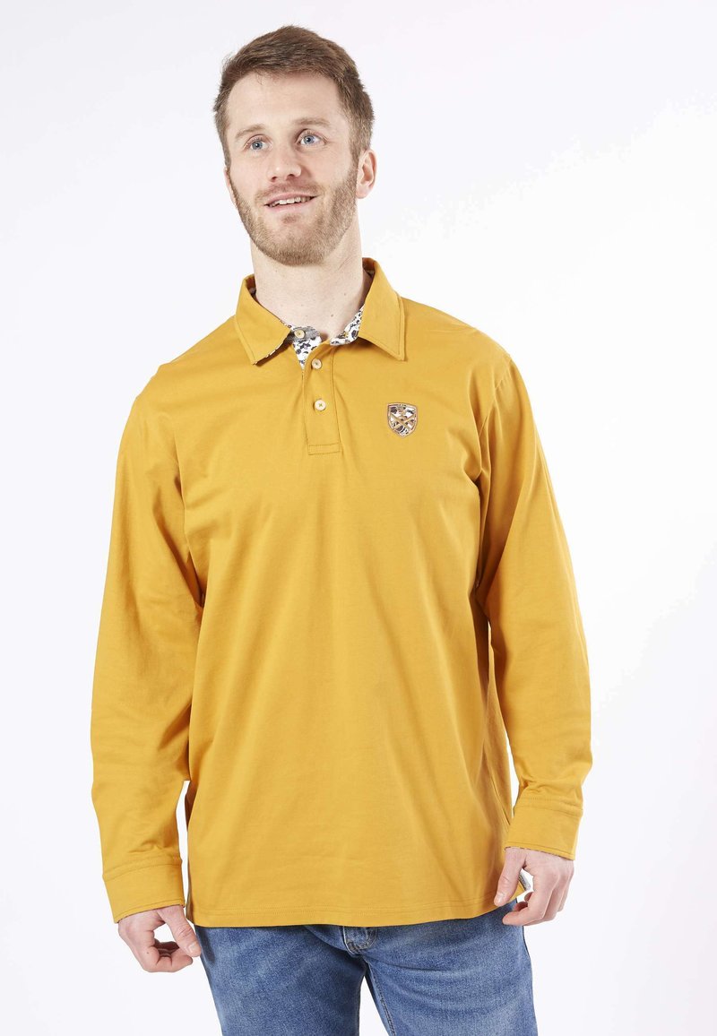 Polo à manches longues en coton jaune moutarde, avec un col à motif et un logo brodé sur la poitrine gauche.