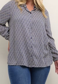 Chemise à manches longues et à boutons en bleu et crème avec un motif géométrique. Présente un col et une coupe décontractée. Tissu doux avec un léger éclat.
