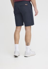 Navy blue chino shorts with a smooth texture, featuring a back pocket and a small label. Worn with white ankle socks and gray sneakers.