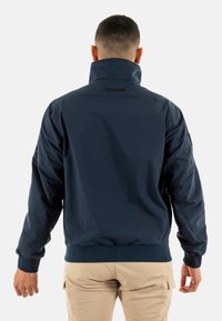 Chaqueta impermeable de color azul marino con un alto cuello, puños elásticos y una cintura ajustada. Textura suave con un brillo sutil.