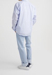 Ljusblå randig skjorta med knappar och långa ärmar, bärs tillsammans med ljusblå jeans och vita sneakers. Avslappnad passform, synliga söm detaljer.