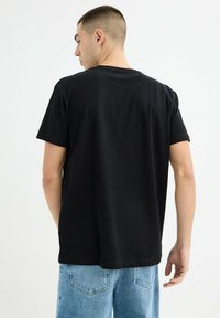 Camiseta de algodón negra con mangas cortas, cuello redondo y un corte relajado, combinada con pantalones cortos de mezclilla azul claro. Detalles de costura visibles.