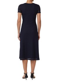 Robe midi bleu marine avec des manches courtes en dentelle, un motif texturé et une jupe évasée. Présente un col rond et un ourlet festonné.