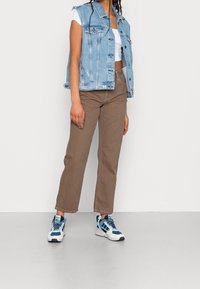 Jeansväst i ljusblått, vit crop top, bruna vida byxor och sportskor med blå och vita detaljer. Enkel, avslappnad outfit.