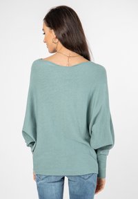 Hellblaugrüner, übergroßer Pullover mit rundem Rückenausschnitt, langen Ärmeln und gerippten Bündchen. Weiche Textur und lockere Passform.