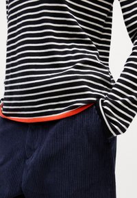 Svart og hvitstripet langermet skjorte med lys orange kant, parret med marineblå kordfløyelsbukser med ribbet tekstur.