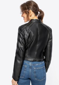 Black leather jacket with studded accents, cropped design, and a smooth texture. Features structured shoulders and fitted long sleeves.