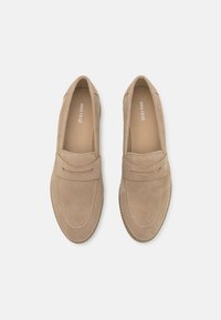 Ljust beige mockask loafers med dekorativ sömnad och ett framband. Slät textur, rund tå och en platt sula.
