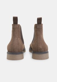 Botine din suede maro, până la gleznă, cu panouri elastice pe lateral, vârf rotund, benzi de prindere în spate și o talpă din cauciuc texturată.