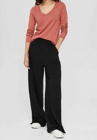Suéter de cuello en V rosa y pantalones de pierna ancha negros. El suéter es acogedor con mangas largas; los pantalones tienen una cintura elástica y una textura suave. Zapatos blancos.