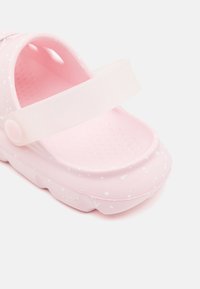 Light pink clogs with a textured surface, white speckles, and a translucent strap. Includes drainage holes for breathability.