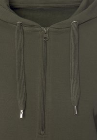Felpa con zip color verde oliva, caratterizzata da lacci testurizzati, una zip metallica e un morbido rivestimento interno. Il design sottolinea comfort e funzionalità.