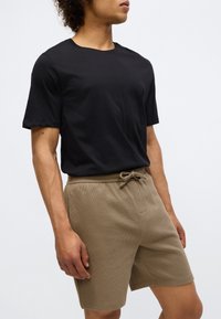 Tricou negru din bumbac cu mâneci scurte, asociat cu pantaloni scurți texturați bej, care au un brâu elastic și detaliu cu șnur.