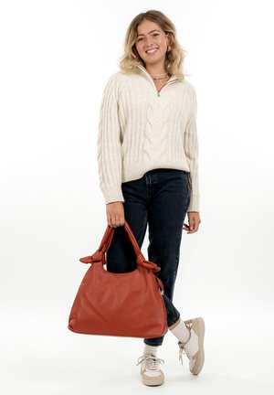 Red leather hobo bag with knotted handles, smooth texture, soft shape, and a spacious, slouchy design, held by a person.