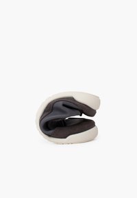 Scarpa piegata con tomaia grigia scura dal tessuto liscio, suola in gomma bianca e design minimalista.