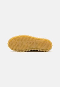 Rubber sneaker sole in yellow, featuring a textured pattern with ridges and a prominent logo embossed in the center.