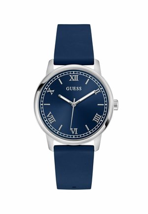 Une montre ronde en marine avec une lunette en argent, présentant des chiffres romains et le nom de la marque "Guess" affiché en évidence sur le cadran.