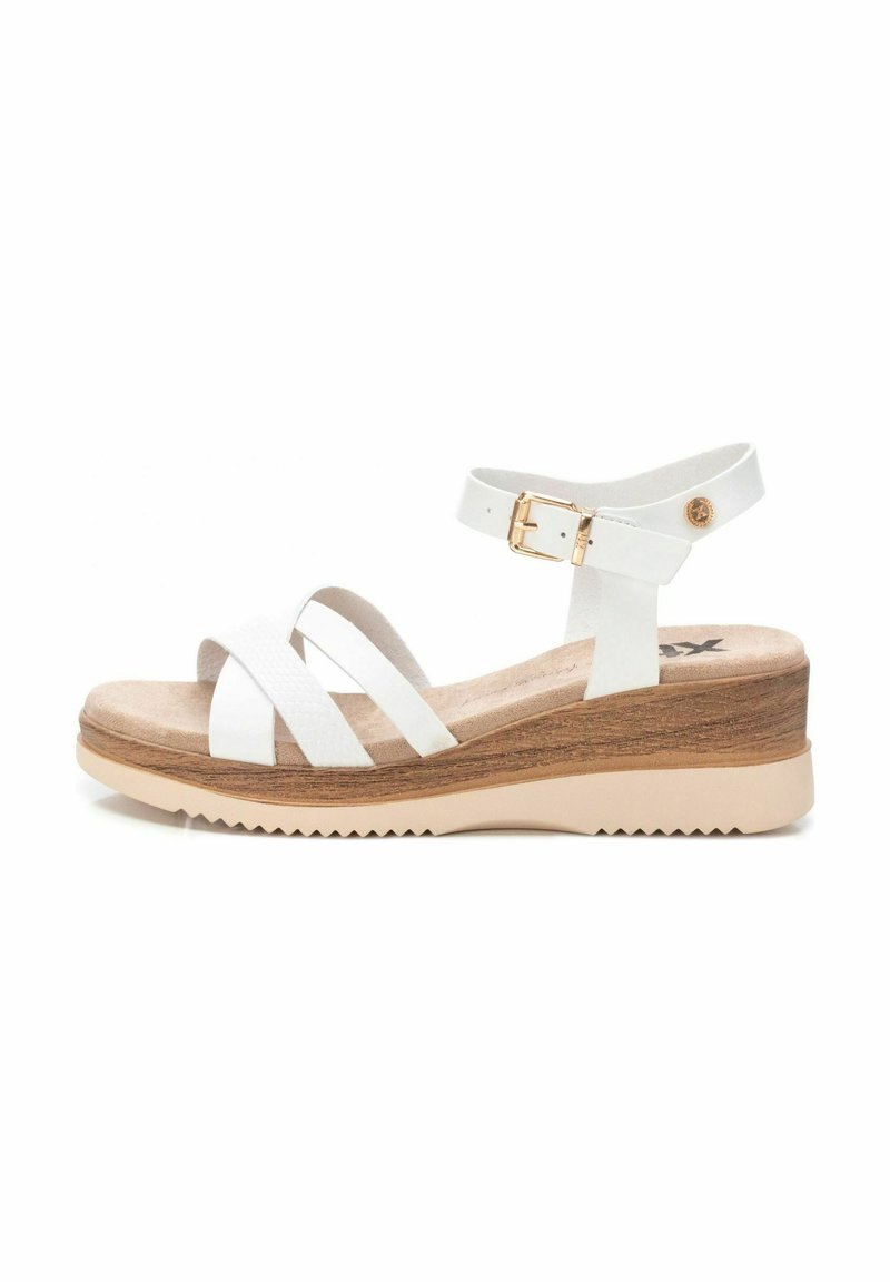 Sandalias de cuña blancas con tiras cruzadas en material sintético texturizado y una correa ajustable en el tobillo. Cuenta con una plataforma similar a corcho y suela de goma.