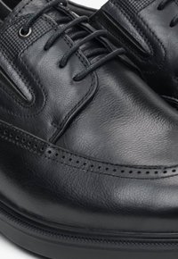 Czarne skórzane buty z gładką fakturą, sznurowanym zapięciem, perforowanymi akcentami na nosku oraz wytrzymałą gumową podeszwą.