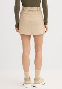 Minifalda de ante color canela con trabillas para cinturón, silueta recta y dos bolsillos traseros. Combinada con zapatos deportivos beige y calcetines claros.