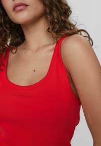 Rød ribbet tanktop med en rund udskæring, tynde skulderstropper og en tætsiddende pasform. Stofser materialet blødt og strækbart ud.