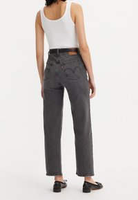 Jeans grises de talle alto con piernas rectas, bolsillos traseros cosidos y una etiqueta de cuero en la cinturilla. Combinados con una camiseta sin mangas blanca.