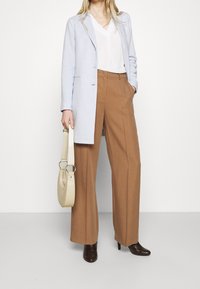 Light blue tailored coat, white v-neck blouse, brown wide-leg trousers, brown heeled boots, and a cream handbag with circular accents.
