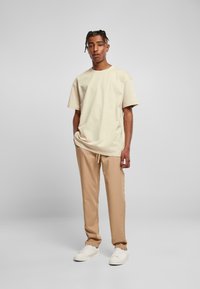 Beige bomull T-skjorte med korte ermer, kombinert med beige joggebukser. Modellen har på seg hvite sneakers. En enkel, avslappet passform.