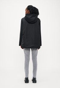 Sort hættejakke med en glat, mat overflade, parret med lysegrå tætsiddende jeans og sorte ankelstøvler. Enkel, funktionel design.