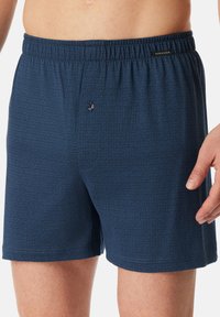 Boxers bleus à motifs avec une taille élastique, un bouton à l'avant et une texture douce arborant un design géométrique subtil.
