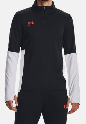 Black and white long-sleeve athletic pullover with red Under Armour logo on chest and black pants with matching logo on thigh.