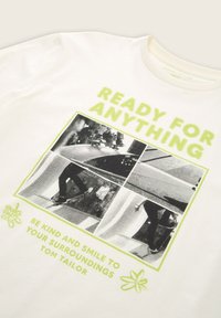 Vit bomulls t-shirt med grön text "READY FOR ANYTHING" och en svartvitt foto collage. Kortärmad med klassisk rund hals.